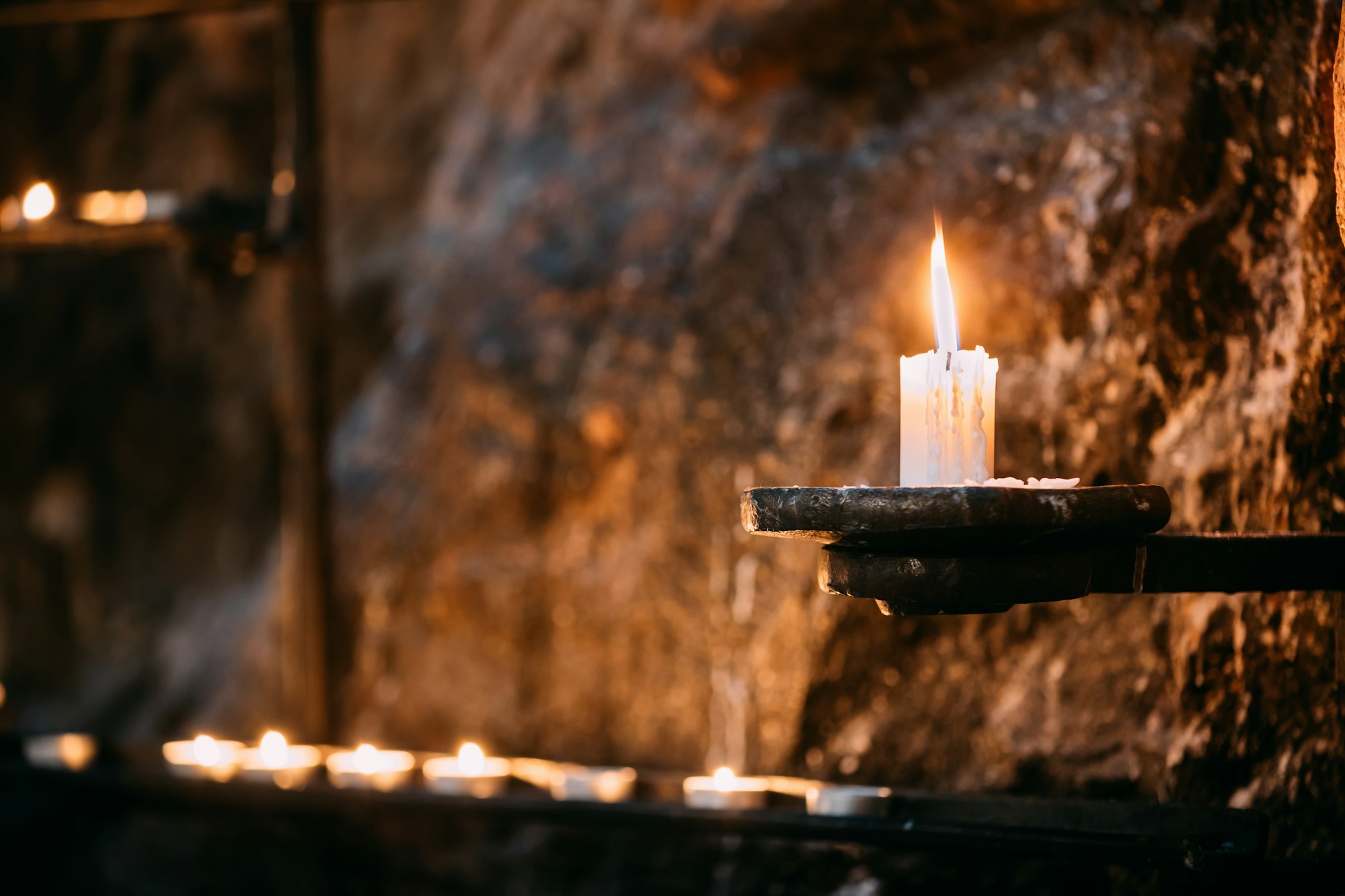 Old Candle In Church. Candle Light Flame Near Ancient Wall